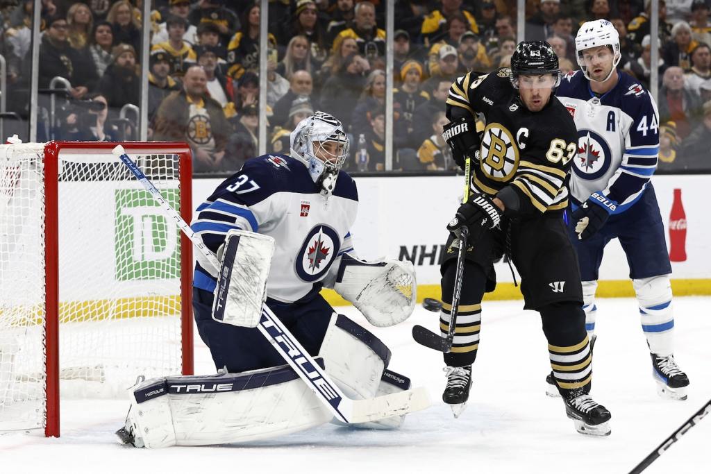 Jan 22, 2024; Boston, Massachusetts, USA; Boston Bruins left wing Brad Marchand (63) tries to deflect a shot on Winnipeg Jets goaltender Connor Hellebuyck (37) during the second period at TD Garden. Mandatory Credit: Winslow Townson-USA TODAY Sports