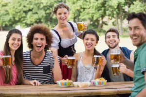 Friends drink beer at a picnic table being waited on by a waitress in traditional Oktoberfest wear.