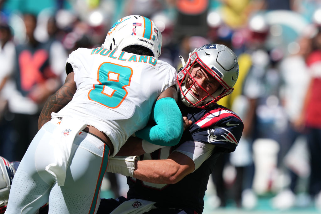 MIAMI GARDENS, FLORIDA - SEPTEMBER 11: Mac Jones #10 of the New England Patriots takes a hit from Jevon Holland #8 of the Miami Dolphins after making a pass in the fourth quarter of the game at Hard Rock Stadium on September 11, 2022 in Miami Gardens, Florida. (Photo by Eric Espada/Getty Images)