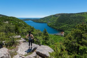 woman atop a hiking trail overlooking a pond in Maine.