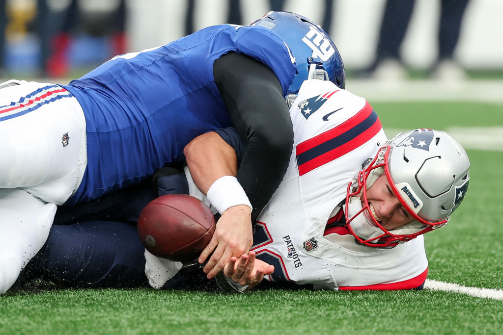 EAST RUTHERFORD, NEW JERSEY - NOVEMBER 26: Mac Jones #10 of the New England Patriots fumbles the ball while being tackled by Kayvon Thibodeaux #5 of the New York Giants during the second quarter at MetLife Stadium on November 26, 2023 in East Rutherford, New Jersey. (Photo by Al Bello/Getty Images)