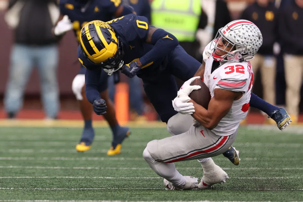 ANN ARBOR, MICHIGAN - NOVEMBER 25: TreVeyon Henderson #32 of the Ohio State Buckeyes takes a hit from Mike Sainristil #0 of the Michigan Wolverines at Michigan Stadium on November 25, 2023 in Ann Arbor, Michigan. (Photo by Gregory Shamus/Getty Images)